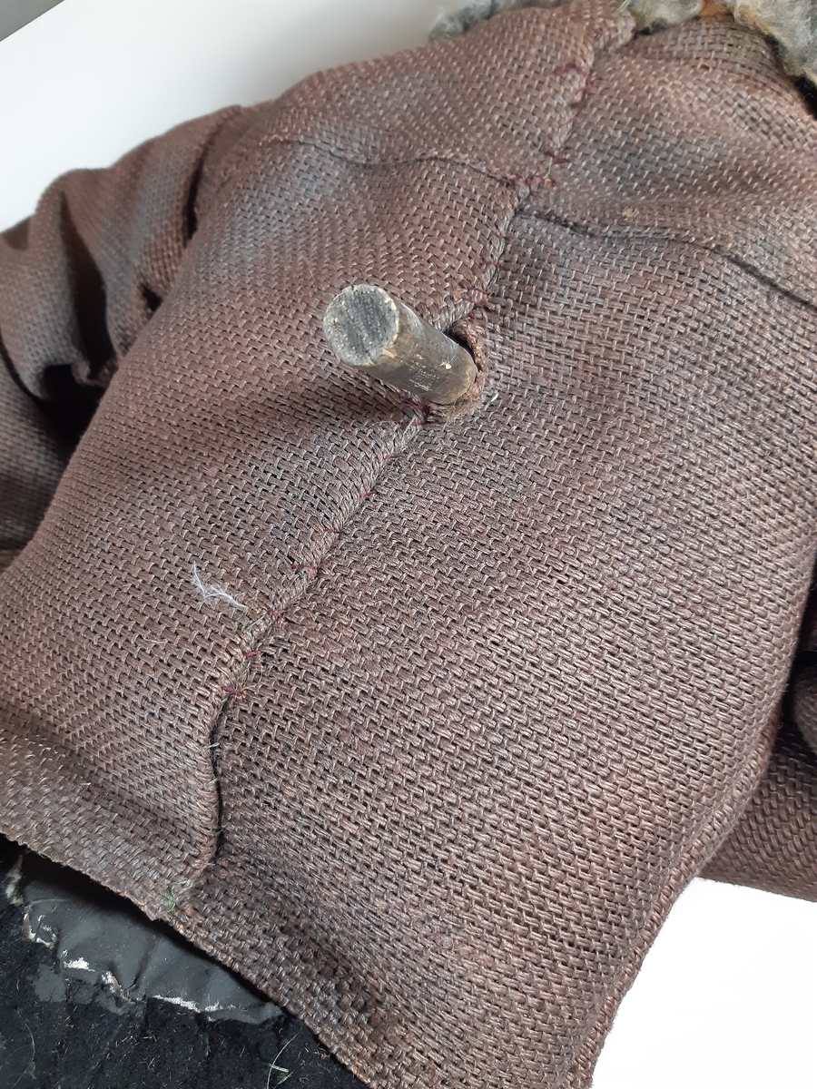 Speldocka föreställande en äldre man med grått hår och mustasch, klädd i mörka skinnstövlar, mörka långbyxor, mörkbrun tjock jacka med grå päls och svart plommonstop. Dockan manövreras med hjälp av skaft i rygg, armar och fötter.
