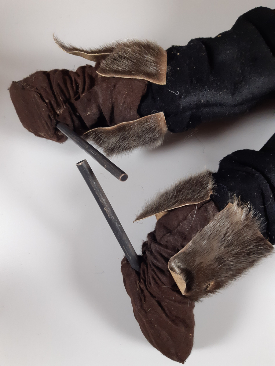 Speldocka föreställande en äldre man med grått hår och mustasch, klädd i mörka skinnstövlar, mörka långbyxor, mörkbrun tjock jacka med grå päls och svart plommonstop. Dockan manövreras med hjälp av skaft i rygg, armar och fötter.
