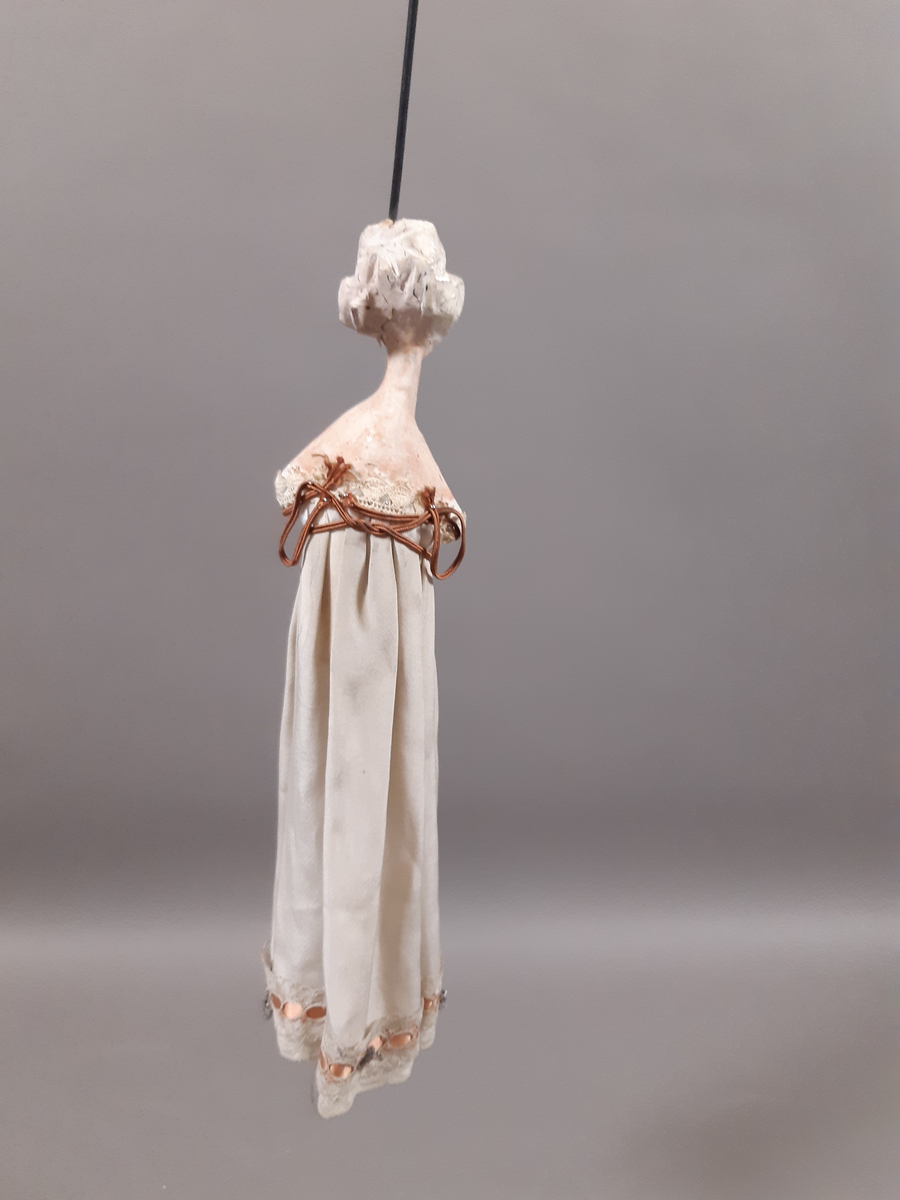 Föreställer en kvinna med vitt hår klädd i vit empirklänning. Dockans armar är lösa. Marionett går att fästa ihop med den andra dockan i dansparet med hjälp av en metallplatta.
