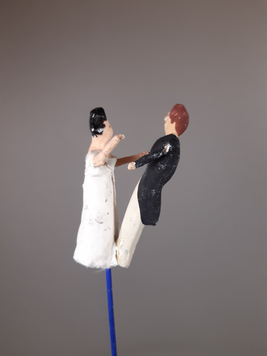 Föreställer en kvinna klädd i vit empirklänning och en man klädd i svart frackjacka, höghalsad vit skjorta och ljusa långbyxor. Kvinnan har svart hår och mannen har brunt hår.
