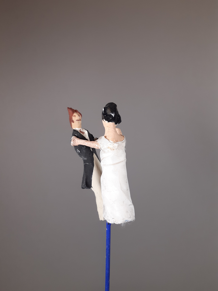 Föreställer en kvinna klädd i vit empirklänning och en man klädd i svart frackjacka, höghalsad vit skjorta och ljusa långbyxor. Kvinnan har svart hår och mannen har brunt hår.
