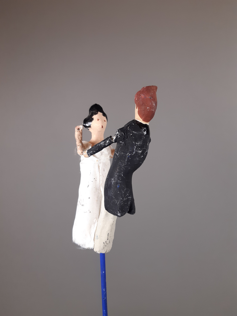 Föreställer en kvinna klädd i vit empirklänning och en man klädd i svart frackjacka, höghalsad vit skjorta och ljusa långbyxor. Kvinnan har svart hår och mannen har brunt hår.
