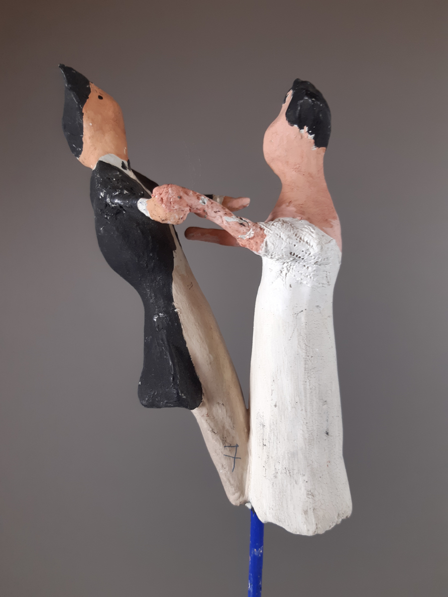 Föreställer en kvinna klädd i vit empirklänning och en man klädd i svart frackjacka, höghalsad vit skjorta och ljusa långbyxor. Både mannen och kvinnan har mörkt hår.
