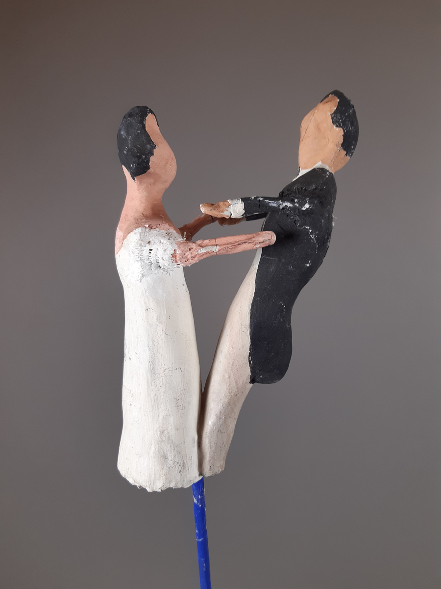 Föreställer en kvinna klädd i vit empirklänning och en man klädd i svart frackjacka, höghalsad vit skjorta och ljusa långbyxor. Både mannen och kvinnan har mörkt hår.
