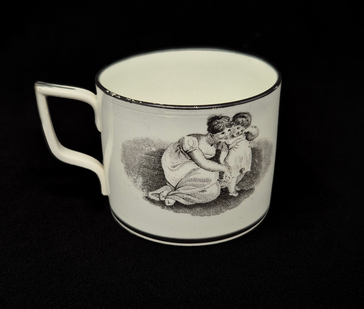 Kaffekopp med fat i pearlware.

Tillverkad i fajans med vit glasyr som har en svag blå ton, typisk för pearlware – en keramisk teknik utvecklad i England av Josiah Wedgwood omkring år 1779. Den blå tonen i glasyren uppnås genom tillsats av kobolt.

Dekoren är utförd med transfertryck och föreställer kvinnor med barn. Motivet är nyklassicistiskt och var vanligt under den tidiga empiren, omkring 1800–1810.

Det är inspirerat av den irländske konstnären Adam Buck (1759–1833), känd för sina idealiserade familjescener.

Troligen tillverkad i Staffordshire, England.