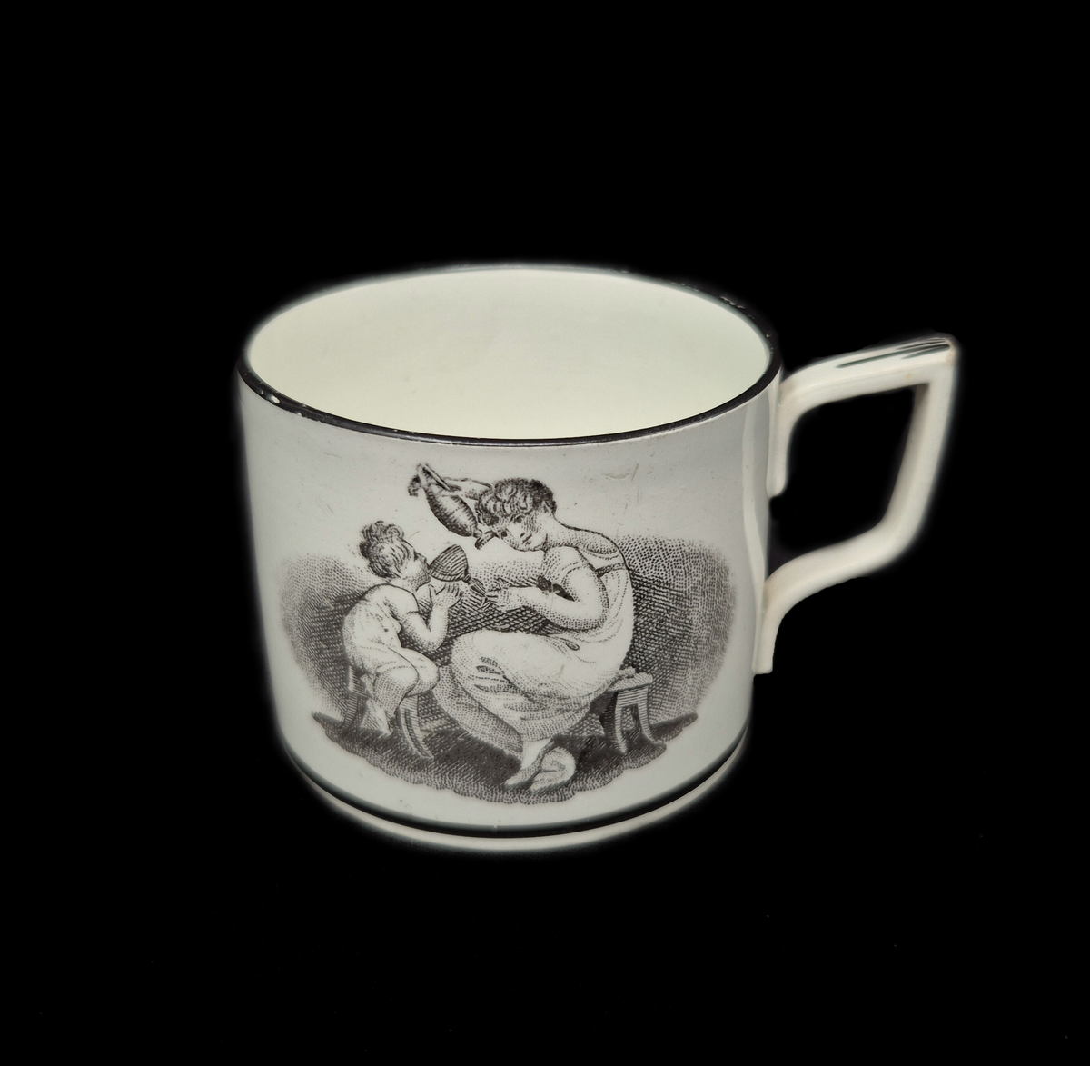 Kaffekopp med fat i pearlware.

Tillverkad i fajans med vit glasyr som har en svag blå ton, typisk för pearlware – en keramisk teknik utvecklad i England av Josiah Wedgwood omkring år 1779. Den blå tonen i glasyren uppnås genom tillsats av kobolt.

Dekoren är utförd med transfertryck och föreställer kvinnor med barn. Motivet är nyklassicistiskt och var vanligt under den tidiga empiren, omkring 1800–1810.

Det är inspirerat av den irländske konstnären Adam Buck (1759–1833), känd för sina idealiserade familjescener.

Troligen tillverkad i Staffordshire, England.