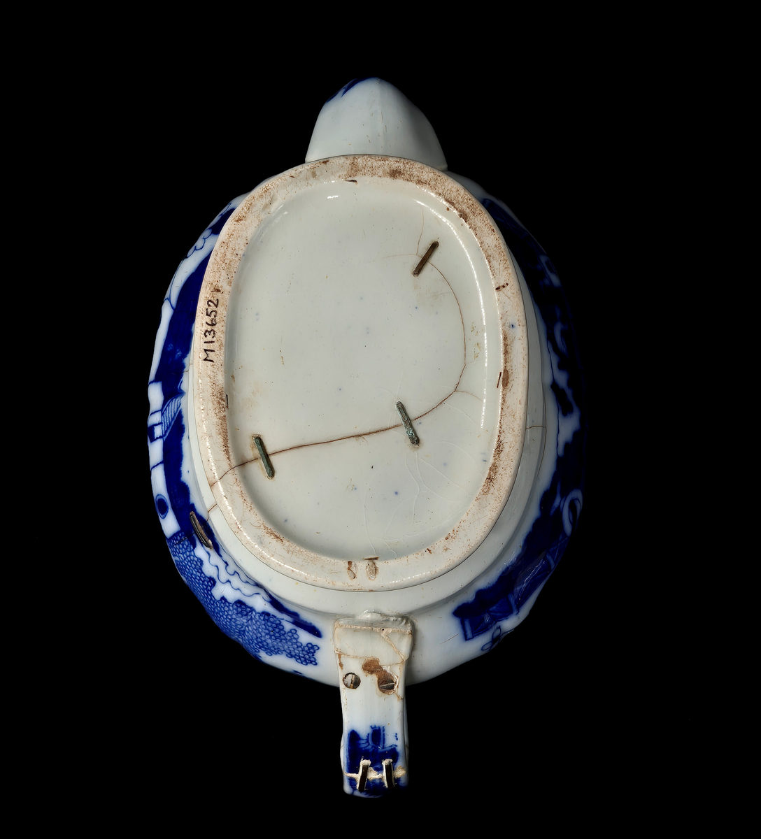 Tekanna, med lock, fajans. Blå kinesimiter mot vit bakgrund. Diverse lagningar med zinkklamrar. 