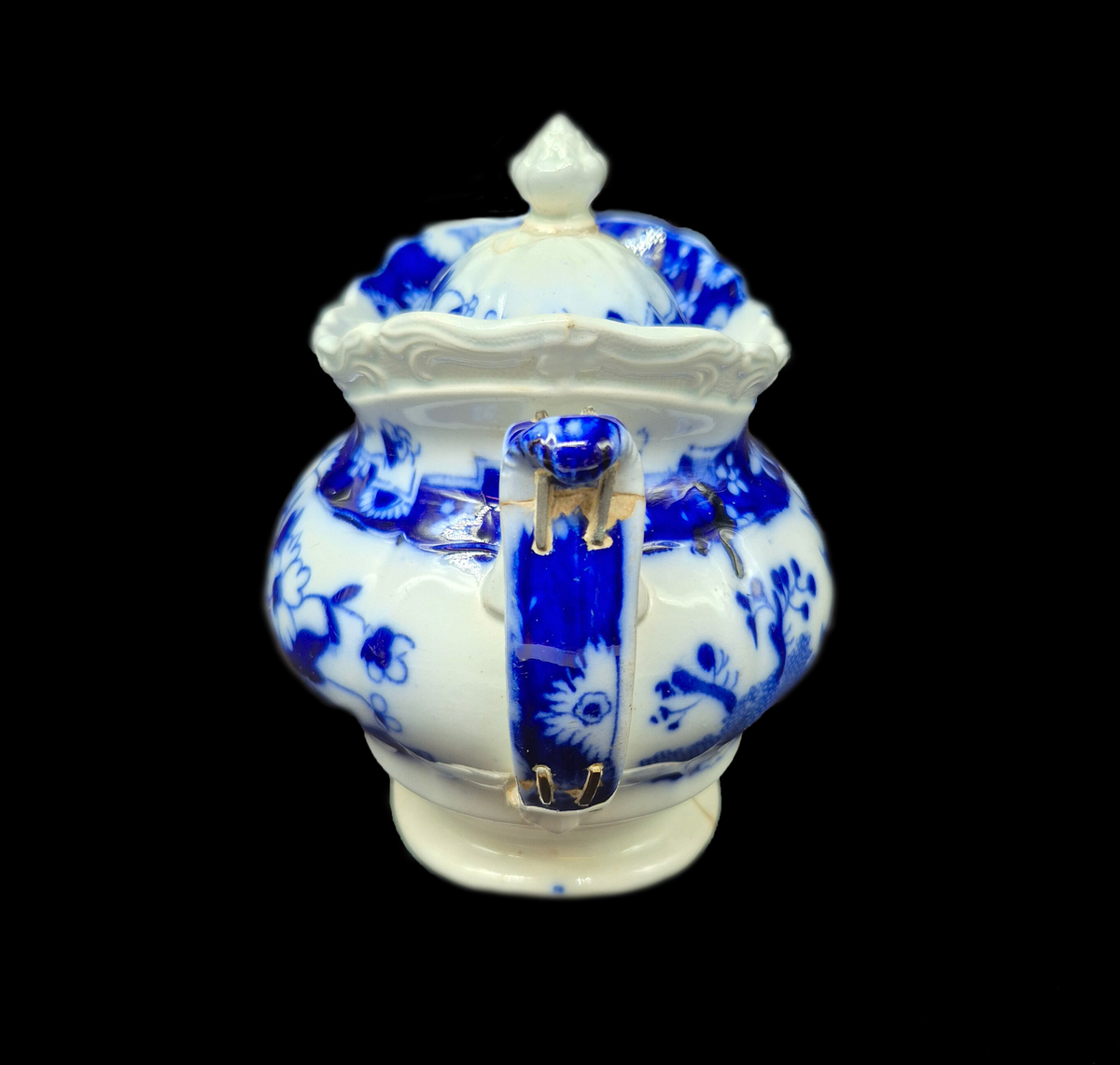 Tekanna, med lock, fajans. Blå kinesimiter mot vit bakgrund. Diverse lagningar med zinkklamrar. 