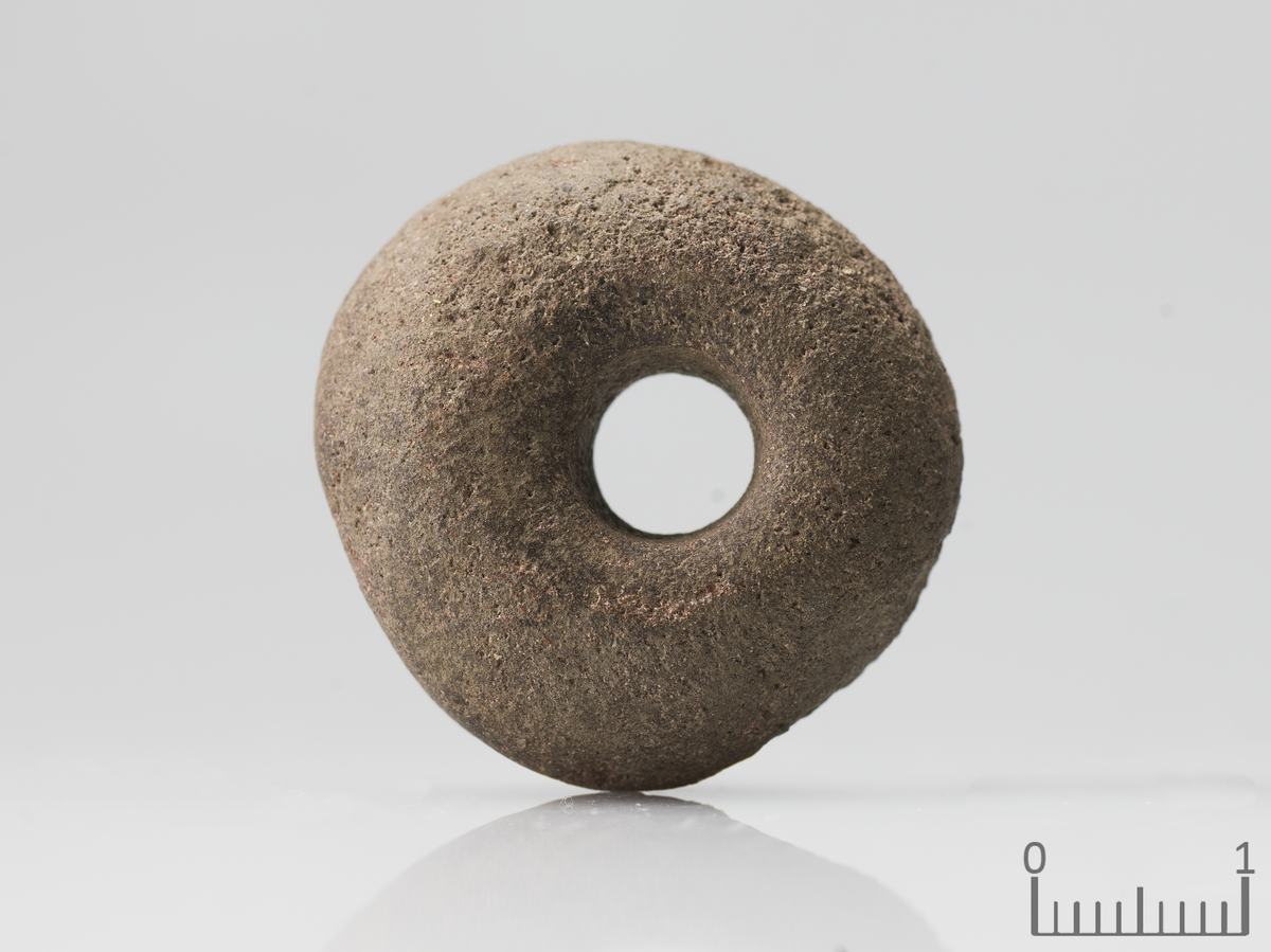 Spinnehjul av sandstein med tilnærma rett basis- og toppflate og konvekse sideflater som type IB/IIC (Hofseth 1985: fig. 7), men forma er asymmetrisk. Teinholet skrår noko frå basis til toppflata. Diam. 29,8 mm, h. 13,6-18,3 mm. Diam. på teinholet 8,9 - 10 mm.