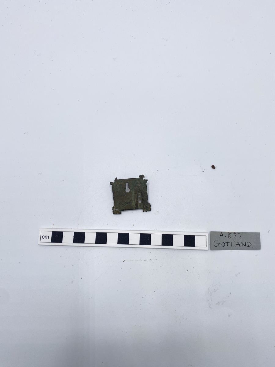 Beslag till lås av brons, närmast kvadratiskt med små bladliknande utskott i hörnen - de två nedre skadade. Kvarvarande nit för fastsättning. Litet nyckelhål, på baksidan kvarvarande låsmekanism
Av mässing, 11/4 tum i fyrkant