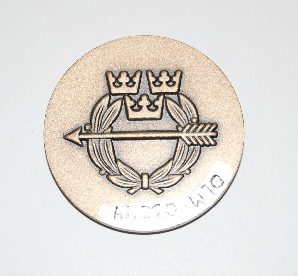 Bronsefarget medalje med motiv av et hode til en ukjent person. Hodet er i profil. Det er også motiv av det som antas å være emblemet til den Frivilliga skytterörelsen.