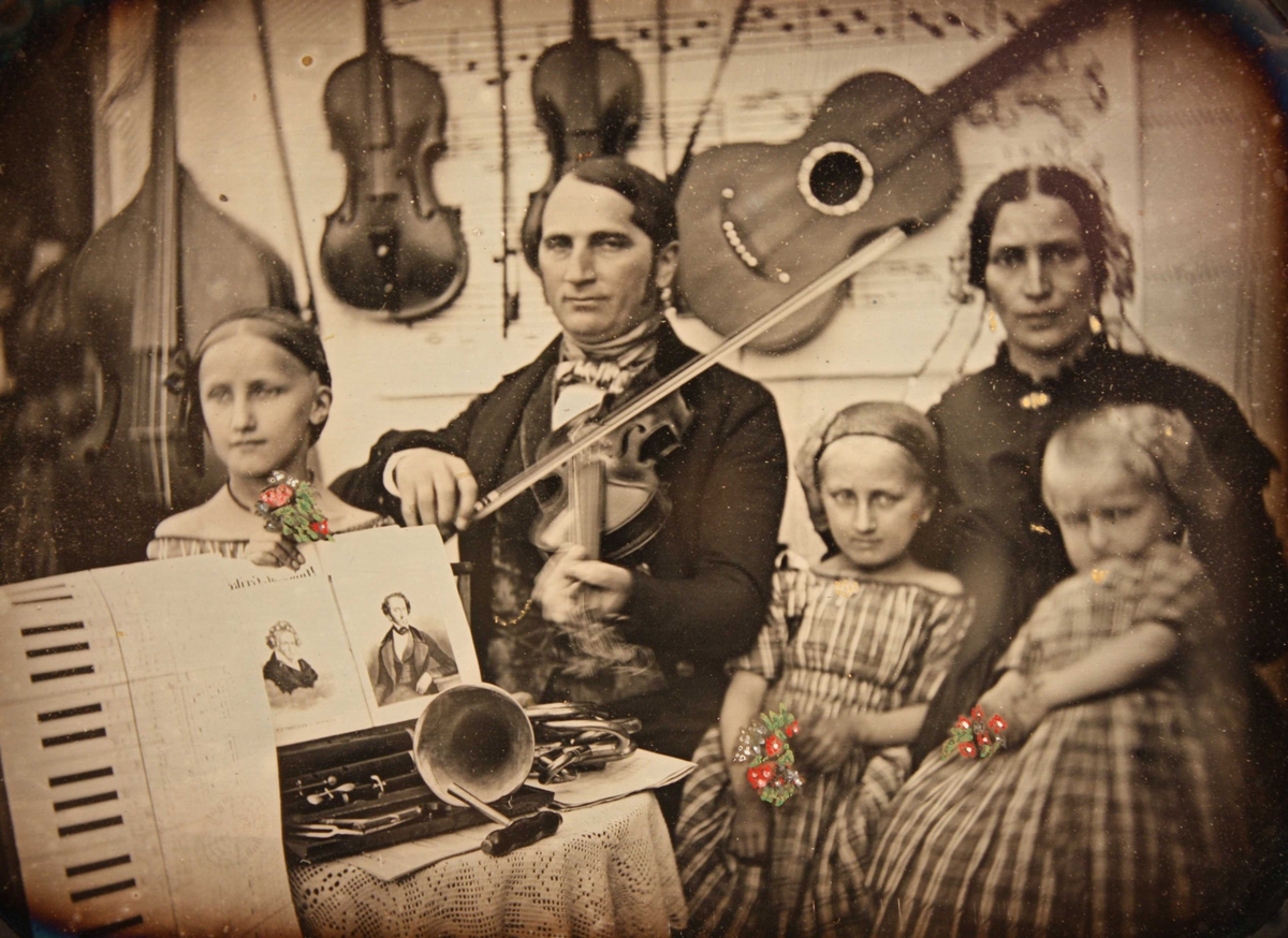 Gruppeportrett av organist Thoschlag  i Arendal med familie, 1852. Mot bakgrunn av musikalier ser man Friedrich Wilhelm  Thoschlag, stadsmusikus i Arendal, og hans hustru  Birgitte Rosina Hachenberg med tre barn: fra v.  døtrene Felicita f. 1842, Birgitte Wilhelmine Camilla  f. 1846, og Betty Cecilie Jenny f. 1849.  Barna holder små malte blomsterbuketter i hendene. 
