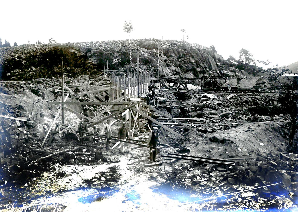 "18/07-1913" Nitriden. Fabrikktomten er planert. Forskaling for omformerstasjon, byggetrinn 1, er i gang. Høyden i bakgrunnen er planert, beregnet for svovelsyrefabrikk, som ikke ble noe av. Tromøysund og Tromøy til høyre.