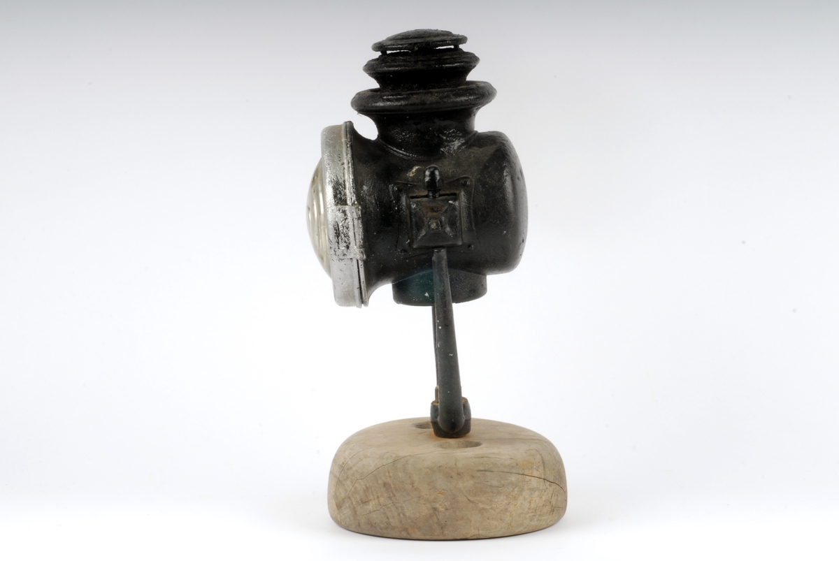 Form: Sylinderformet lykt med rundt glass i fronten.
Stativ av jern satt ned i foten. Oljedrevet til lampe før 1914 i Tyskland