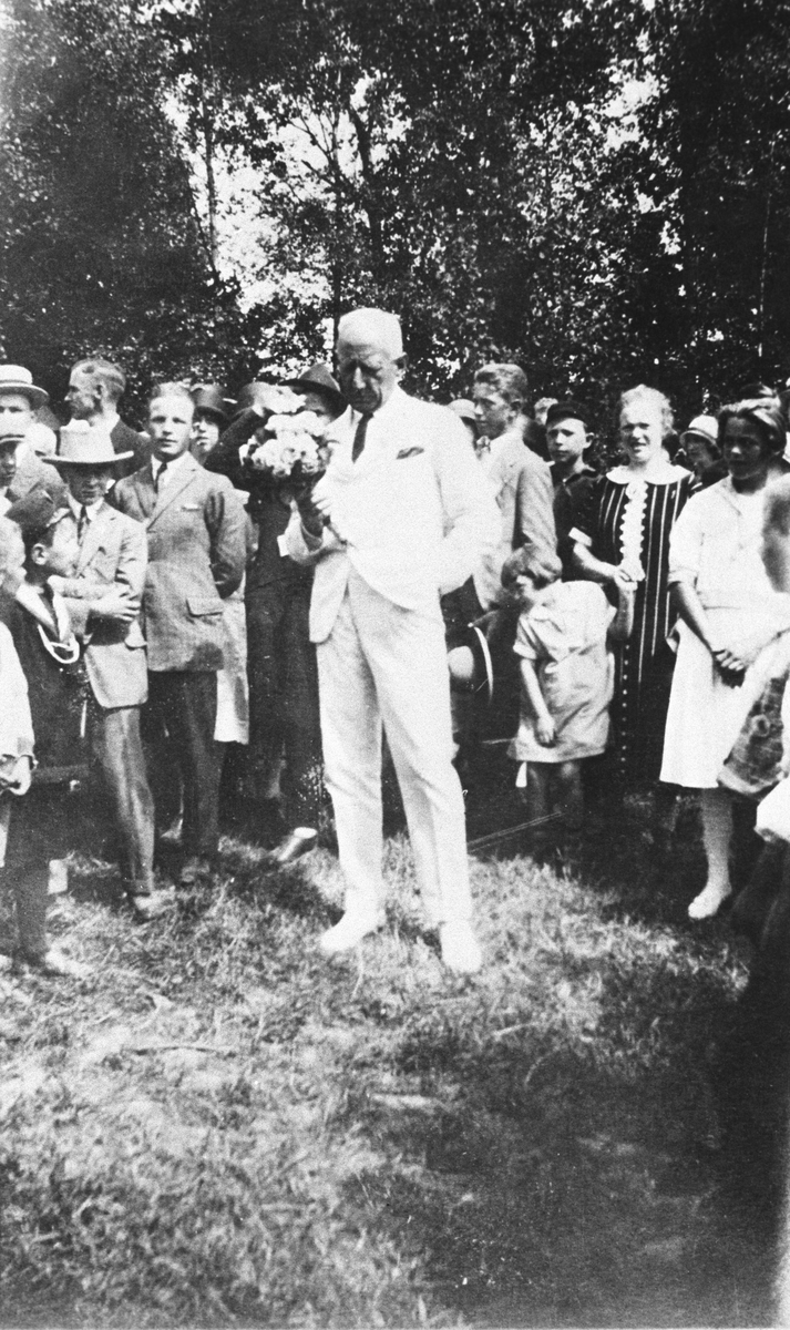 Roald Amundsen med blomster midt i en forsamling voksne og barn