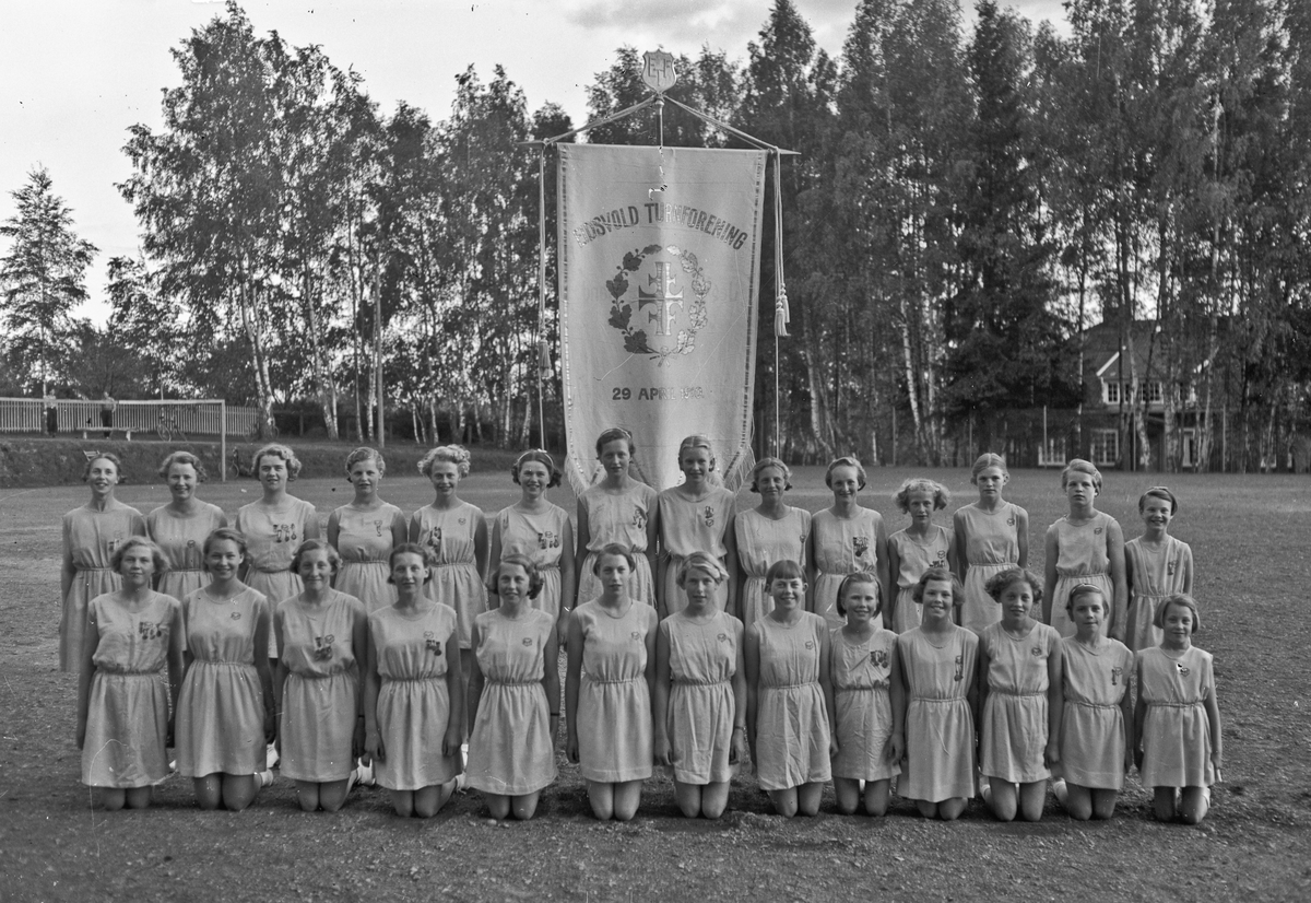 27 jenter foran fanen til ”Eidsold Turnforening 29. april 1910”. Sannsynligvis fra turnstevne i ca. 1937. En av jentene heter Skjervum.