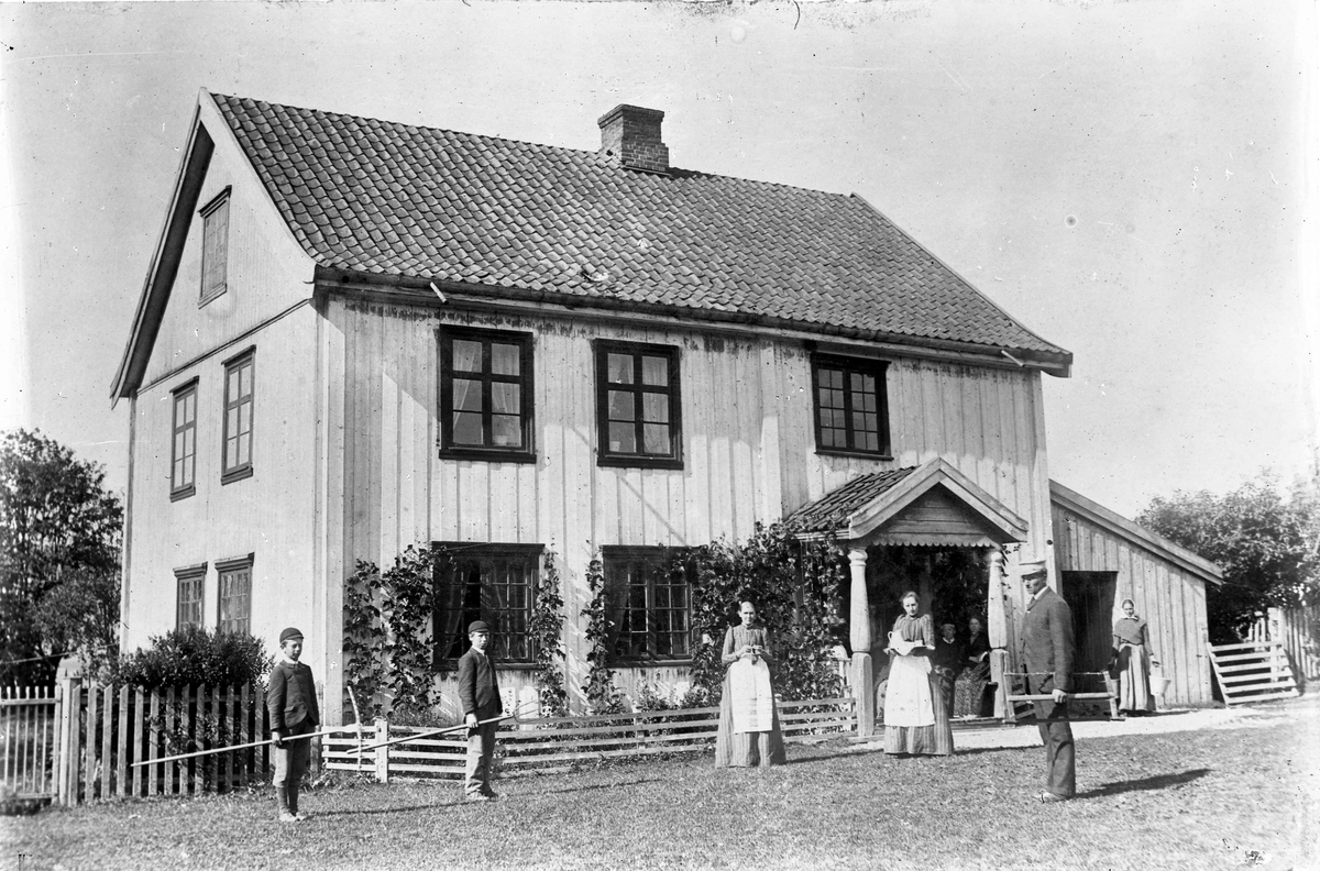 Barn og voksne med river utenfor et hus. I høyonna. 
18.04.2013:
Bildet er fra Bårli gård.
Skrevet av: Trond Gundersen