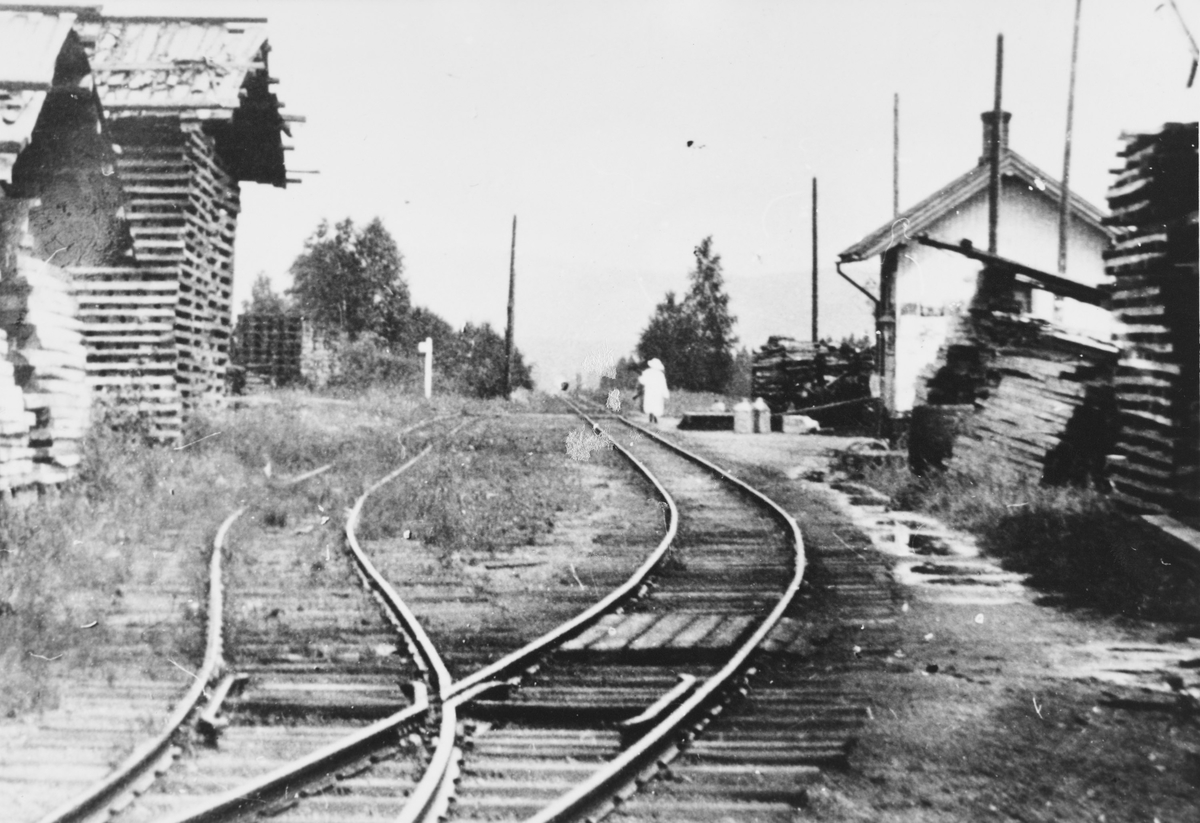 Ved- og plankelagre som venter på transport, trolig under krisen i 1918. Det pågår oppsetting av stolper for elektrisk belysning. Stasjonen har fremdeles utvendig parafinbelysning.