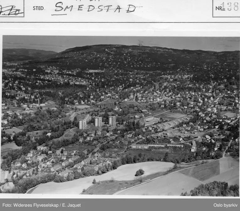 Panoramabilde. Konventveien. Hoffsbyen (hageby), Høyblokkene på Hoff. Smestad skole. Åker, dyrkede jorder. Holmenkollåsen i bakgrunnen. Billedtittel er villedende, da hovedmotiv er Hoff og Heggeli. (Flyfoto)