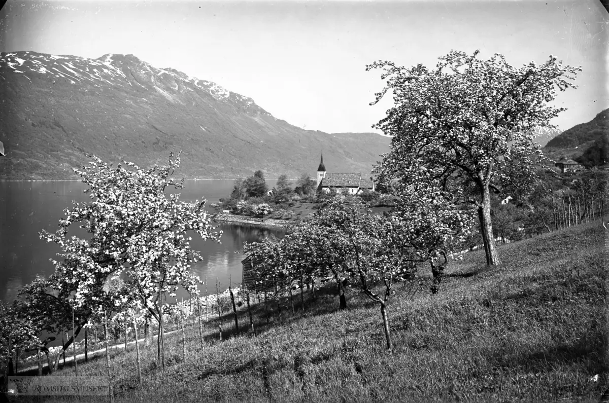 Ullensvang kirke med sørfjorden østover. W:"Ullensvang kirke (Ullensvang kyrkje) er en langkirke fra 1300 i Ullensvang kommune, Hordaland fylke..Byggverket er i mur og stein og har 450 plasser..Bygd i perioden 1250-1300, engelsk gotikk.Arkitekt 1958: A.Arneberg"