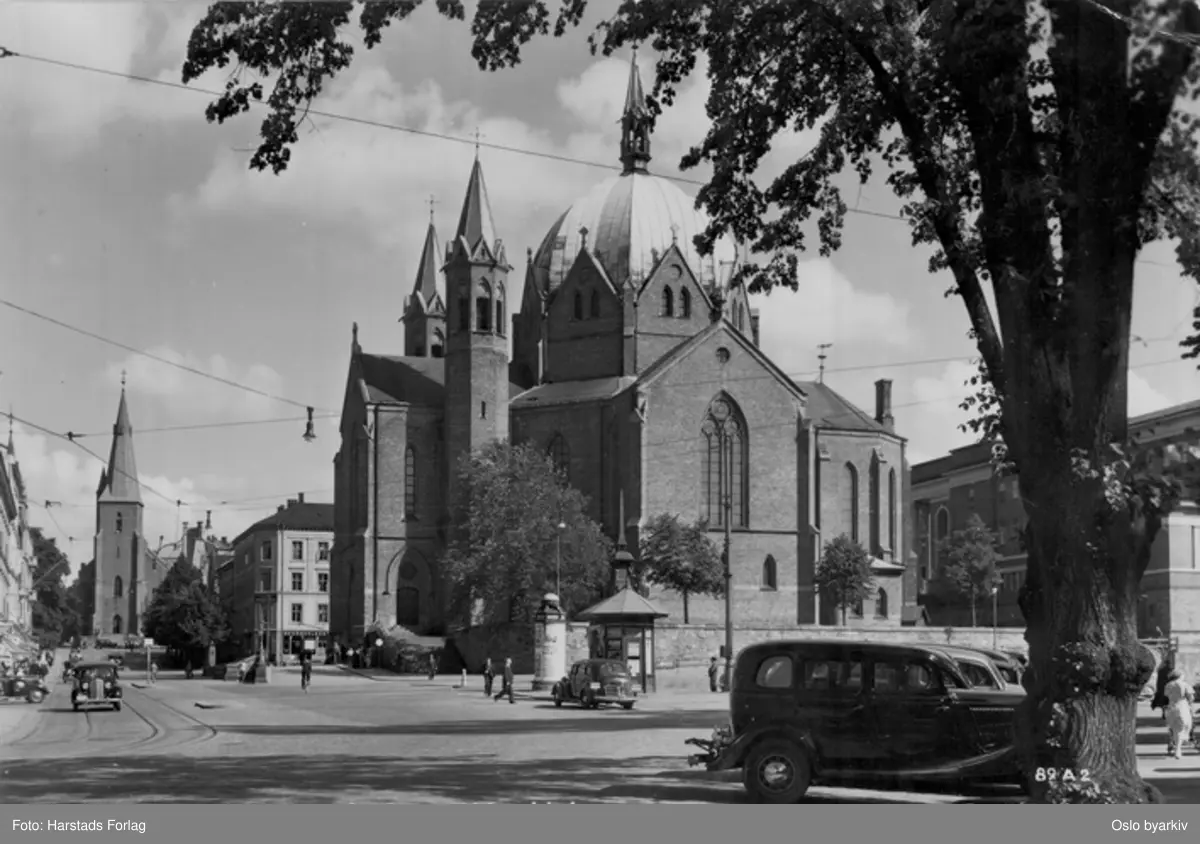 Akersgata ved Arne Garborgs plass og Trefoldighetskirken opp mot St. Olavs kirke. Biler. Narvesens tårnkiosk, reklamesøyle / nedstigningstårn. Postkort 89 A 2.
