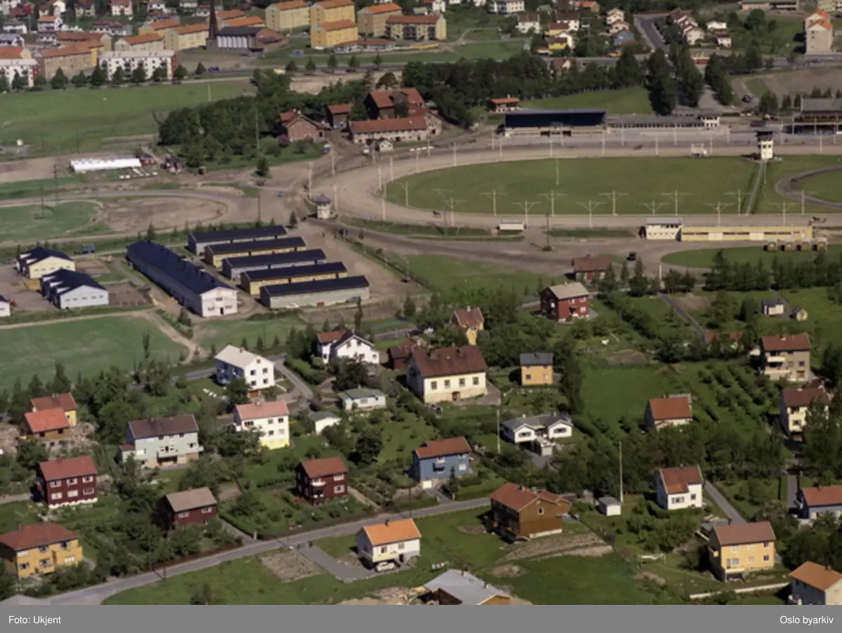 Bjerke travbane, Bjerke gård. Gruppen hus med svarte tak er staller tilhørende Bjerke travbane. Gul bygning midt på bildet er staller for tilreisende hester. Økernveien, Lundliveien, Skogvollveien (Flyfoto)