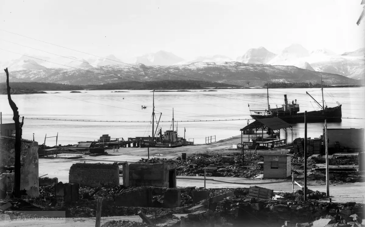 Molde etter bombing 1941. Båten "Eystein - Norge" på fjorden. .Fiskehandler A.Simonsen med sønner i skuret i bakgrunnen midt på bildet.