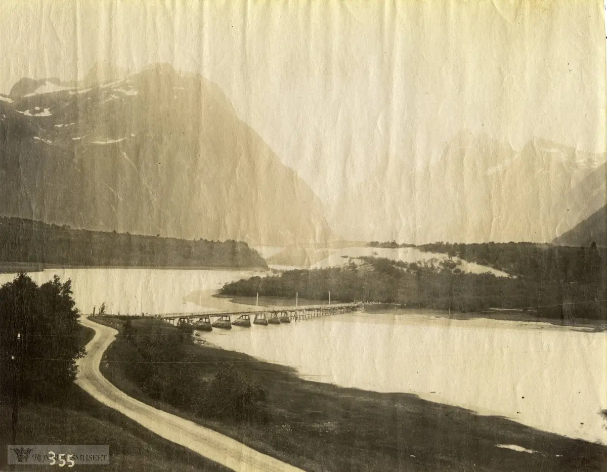 Vi ser Grøttør bru som krysser elva Rauma ca. to kilometer fra Åndalsnes sentrum. Brua var sentral i veinettet gjennom mange tiår, både lokalt og for gjennomgangsveien Dombås-Ålesund. I 1963 åpnet ny bru 1-2 kilometer lengre ned mot elveosen, nær Veblungsnes. Gjennomgangsveien, i dag E136, ble lagt om, og ny trase på andre siden av elva, på venstre side på bildet. Grøttør bru ble etter hvert stengt for biltrafikk og fungerer som gang- og sykkelvei..Bak til høyre på bildet går Isterdalen oppover mot Trollstigen. På høyre side av dalen skimtes de kjente fjelltoppene Bispen, Kongen og Dronninga. Romsdalen går oppover til venstre, og utenfor bildet.