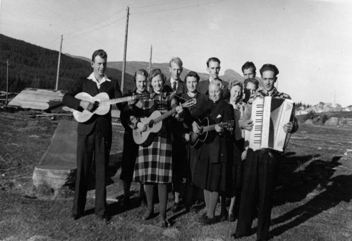 Gruppebilde,gitar,trekkspel,kjole,bukse og jakke.