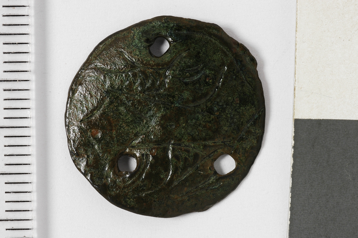 MALV: DIAM. 21 MM, TILNÆRMET FLAT MED TRE HULLER FOR FESTE. 1 STIFTSITTER IGJEN. DEKOREN ER UTYDELIG. REF. FINGERLIN FIG. 402. 