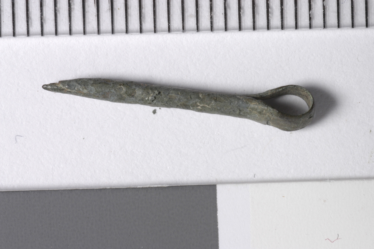 MALV: L. 19  B. 2, 5 MM, ET 2, 5 MM BÅND ER BØYET DOBBELT. DET SMALNER AV MOTBØYEN OG DANNER ET ØYE. SPISSEN ER DANNET VED AT DEN BREDESTE BÅND-HALVPART BRETTES PÅ BEGGE KANTER OM DEN SMALE HALVPART. TORNEN ER HUL !