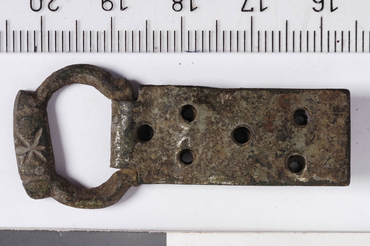 MALV: H. 20 MM L. 47 MM, SVAKT OVAL, PROFILERT RAMME. FORTYKKET FELT DEKORERTMED EN STJERNE AV TRE KRYSSENDE LINJER. BESLAGET ER REKTANGULÆRT, BØYDOM STOLPEN I SPENNEN MED FEM NAGLEHULL OG HULL TIL FORMEN. 