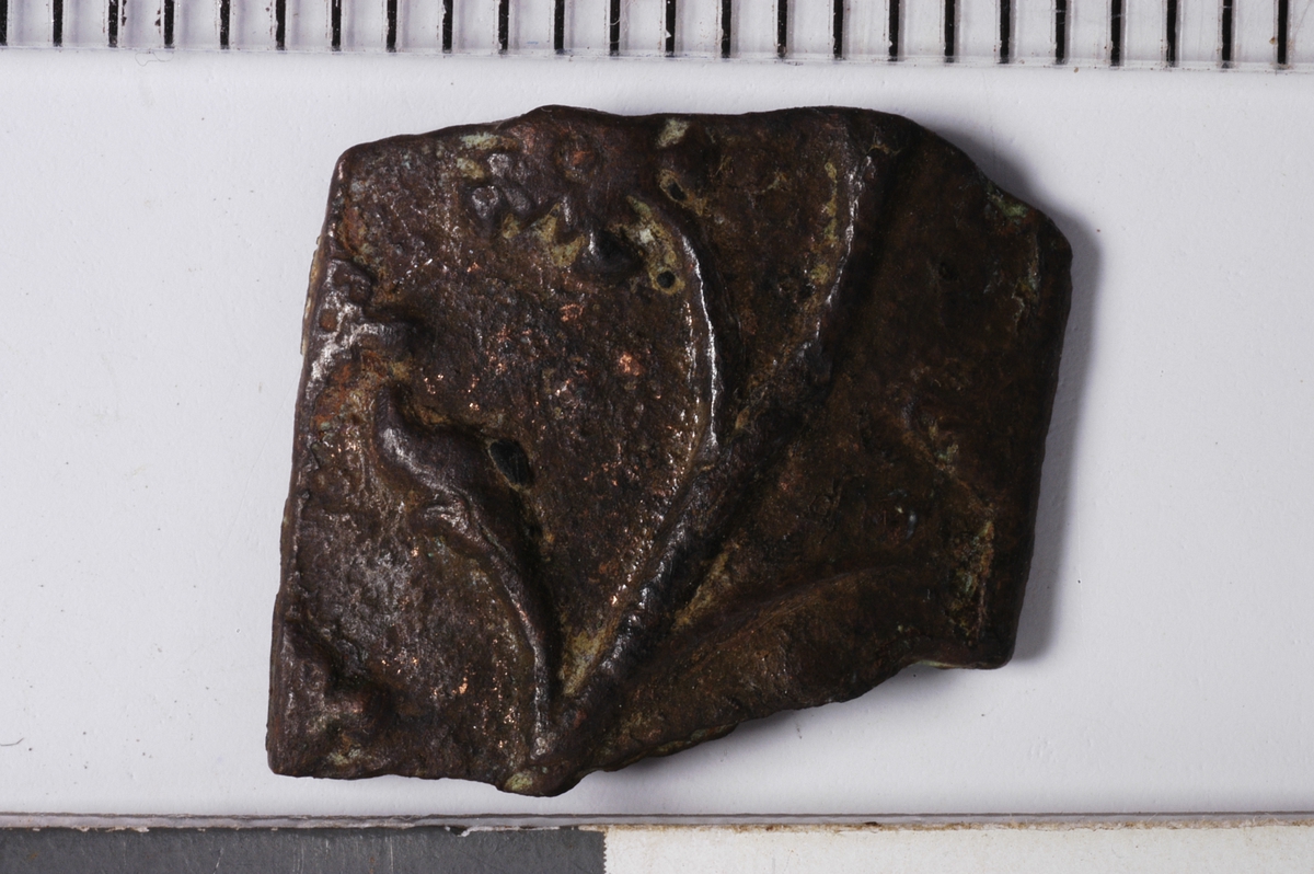 MALV: H. 11 MM B. 12 MM, LITEN, SVAKT BUET PLATE. AVBRUKKET PÅ TO SIDER. OPP-HØYET PLANTEORNAMENTIKK. 