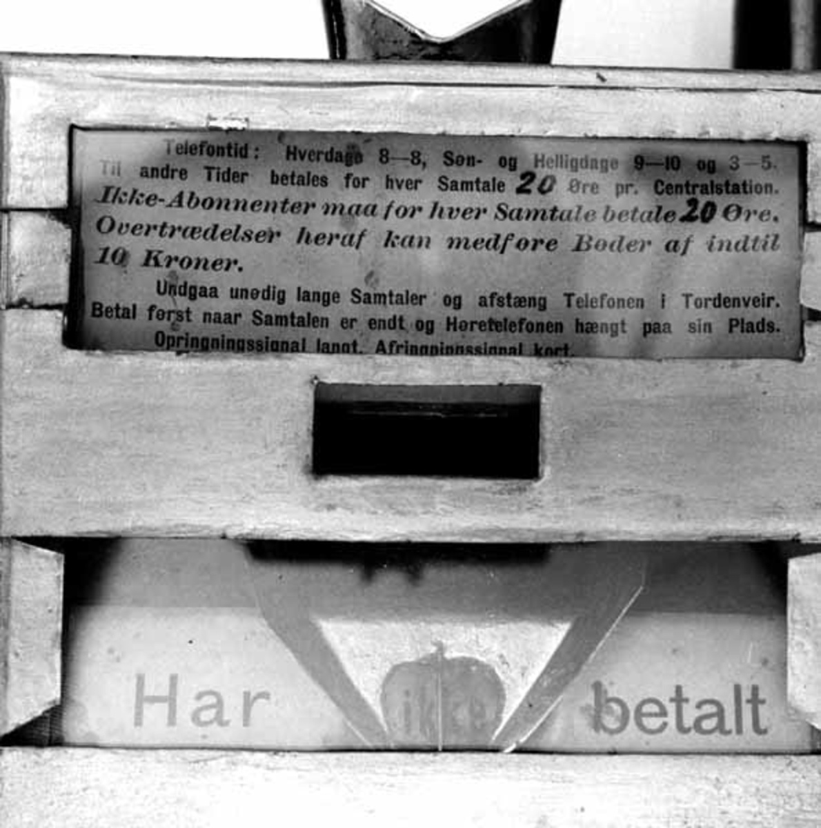 Kasse for myntbetaling av telefonsamtaler, konstruert og patentert av Eberhard Kokkin (1856-1920) i 1895. Innretningen er lagd som en rektangulær blikkboks - 18,2 X 12,5 X 7,3 centimeter, med tre glassvinduer på den flatsida som skal vende fram. Bak det øverste av dem er det innlagt et ark med følgende trykte tekst: «Telefontid: Hverdage 8-8, Søn- og Helligdage 9-10 og 3-5. Til andre Tider betales 20 Øre pr. Centralstation. Ikke-Abonnenter maa for hver Samtale betale 20 Øre. Overtrædelser heraf kan medføre Bøder af indtil 10 Kroner. Undgaa unødig lange Samtaler og afstæng Telefonen i Tordenveir. Betal først naar Samtalen er endt og Høretelefonen lagt paa sin Plads. Opringningssignal langt. Afringningssignal kort.» Det midtre glassvinduet gir bare et innblikk i ei mørk kasse, antakelig der myntene skulle lande. Det nedre vinduet viser inn på ei skrå flate med et ark hvor det står «Har» og «betalt». Mellom disse ordene er det ei renne for mynt. På denne renna er det plasser en liten lapp med ordet «ikke». I den nedre enden av kassa er det en beholder av blikk - 12,2 X 7,3 X 7,2 centimeter - med en messingknapp av en type som ofte ble brukt på skuffefronter sentralt på undersida. I tverrendene av den ytre kassa og skuffen er det rektangulære spalter for en 14,7 centimeter lang jerntein som stikkes gjennom, og låses ved hjelå av et lite hengelås av messing i et hull i enden av jernteinen. Nøkkel til låset er vedhengt. På innsida av skuffens ene endevegg er det for øvrig ei lita trakt, som skal gjøre det enklere å stikke teinen inn riktig. På toppen av kassa er det ei innkastspalte for mynter. Diagonalt på den ene sida av kassa er det et rør som omslutter ei ståltrådhekte. På baksida av kassa er det påloddet fire bandjern med hull for oppskruing på vegg. Sentralt på frontens nedre del har konstruktøren loddet på en liten mynt med teksten «E. KOKKOIN PATENT  AASTA ST.» Ytterflatene på kassa er svartlakkerte, med inntak av fronten, som er gullfarget.