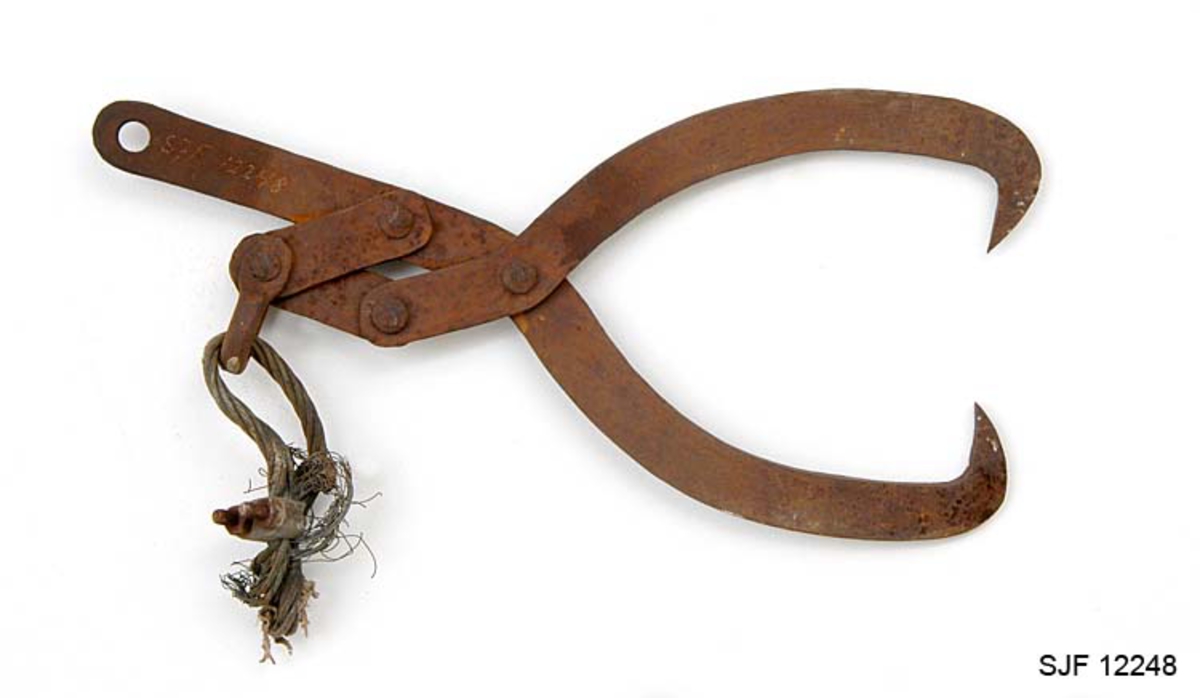 Tømmersaks, brukt til å heise opp tømmerstokker under lessing for transport. Mekanismene her minner om de saksene som ble brukt som håndredskaper i skogen, men dimensjonene er langt kraftigere og solidere. Denne saksas armer er lagd av 1,1 centimeter tjukt platestål. Disse to elementene er sammenføyd ved hjelp av ei kraftig nagle i krysningspunktet. Den nedre delen av armene "buer" mot hverandre og ender i cirka 5 centimeter lange innovervendte pigger, som kløp seg godt fast i yteveden på tømmerstokkene. De øvre endene av armene har ulik lengde. Den ene er 26,5 centimeter lang fra hengslingspunktet, den andre bare 9,5 centimeter. Cirka 8 centimeter fra krysningspunktet mellom de to armene er begge pånaglet "blekker" - om lag 12 centimeter lange og drøyt 3,5 centimeter brede jernband - som møtes i overenden, der det er festet ei solid jernbøyle med ei gjennomgående nagle. I denne bøyla sitter det en rest av et ståltau med diameter 1,2 centimeter. Endeløkka på ståltauet har vært holdt ihop av ei vaierklemme med to strammemuttere. Det må ha vært i dette ståltauet de tunge tømmerstokkene ble heist opp. I den øvre enden av den lengste saksearmen er det et gjennombrutt hull. Her har det antakelig vært festet et annet tau, som man kunne rykke i, slik at tømmerstokkene løsnet når de befant seg i ønsket posisjon.