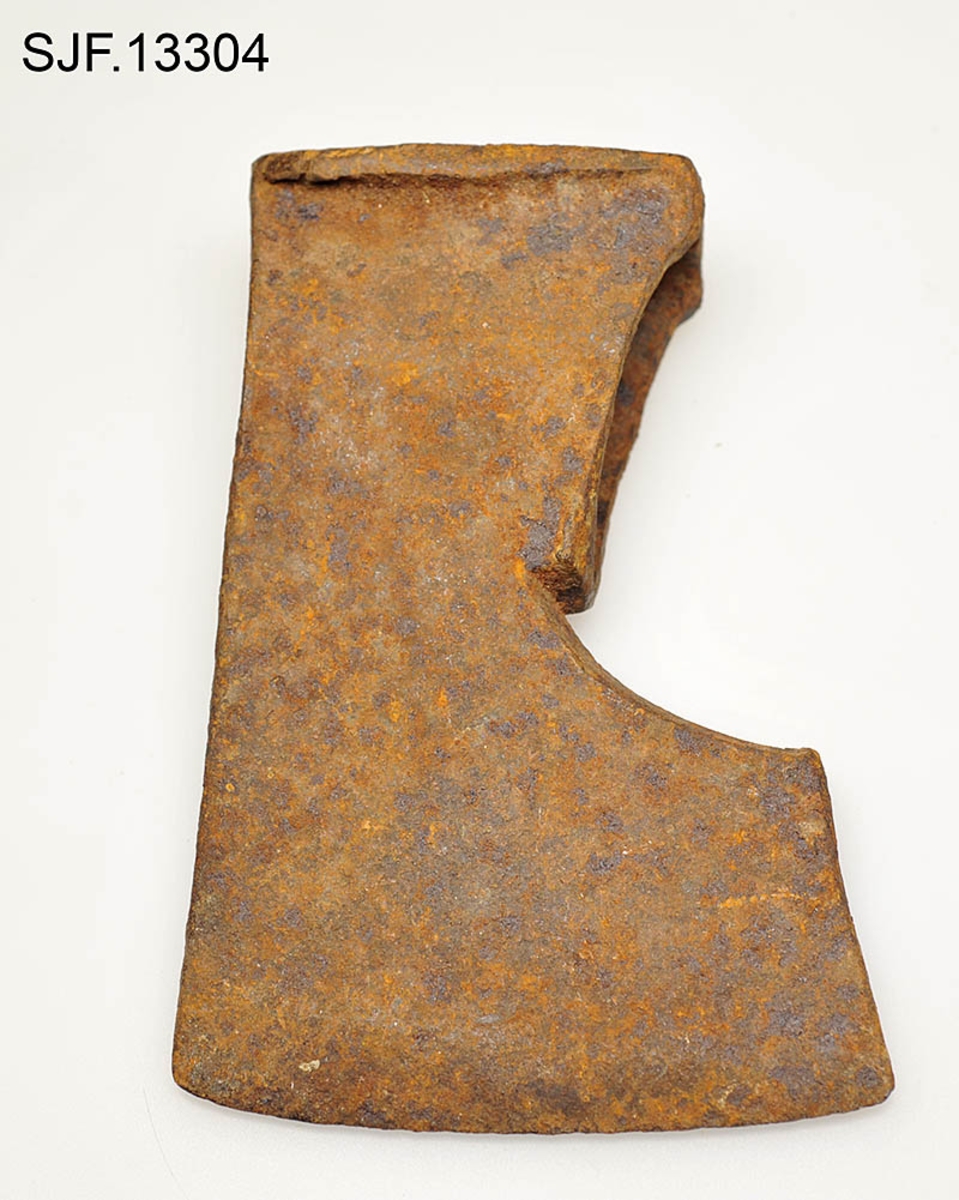 Økseblad uten skaft.  Redskapet er overført fra Borgarsyssel museum i Sarpsborg, dessverre uten proveniensinformasjon ut over at den skal være brukt i Østfold. 

Øksa er smidd, antakelig med innlagt stål i eggpartiet, men ettersom overflata er dekt av rust er det vanskelig å verifisere dette uten å foreta oppsliping.  Dette framstår som et forholdsvis tungt og bredt økseblad.  Med denne bladbredden har det neppe har vært beregnet på hogst, men det kan naturligvis ha vært brukt til barking, men også til ymse håndverksaktiviteter.  Den øvre delen (omkring øyet og nakken) er preget av slitasje.  Det nedenforliggende bladet er noe bredere.  Nakkedelen har opprinnelig vært flat og rektangulær, men den er brukt som hammer, noe som har ført til at godset er noe deformert og at det har dannet seg "skjegg" langs langsidene.  Øyet (skafthullet) har et dråpeformet tverrsnitt (cirka 5, 2 X 2, 6 centimeter). Godset mellom øyet og hammerflata på øksenakken er sprukket, noe som kan ha vært årsak til at redskapet ble kassert.  Eggdelen har betydelig større bredde enn nakkedelen. 