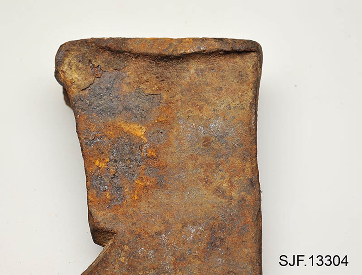 Økseblad uten skaft.  Redskapet er overført fra Borgarsyssel museum i Sarpsborg, dessverre uten proveniensinformasjon ut over at den skal være brukt i Østfold. 

Øksa er smidd, antakelig med innlagt stål i eggpartiet, men ettersom overflata er dekt av rust er det vanskelig å verifisere dette uten å foreta oppsliping.  Dette framstår som et forholdsvis tungt og bredt økseblad.  Med denne bladbredden har det neppe har vært beregnet på hogst, men det kan naturligvis ha vært brukt til barking, men også til ymse håndverksaktiviteter.  Den øvre delen (omkring øyet og nakken) er preget av slitasje.  Det nedenforliggende bladet er noe bredere.  Nakkedelen har opprinnelig vært flat og rektangulær, men den er brukt som hammer, noe som har ført til at godset er noe deformert og at det har dannet seg "skjegg" langs langsidene.  Øyet (skafthullet) har et dråpeformet tverrsnitt (cirka 5, 2 X 2, 6 centimeter). Godset mellom øyet og hammerflata på øksenakken er sprukket, noe som kan ha vært årsak til at redskapet ble kassert.  Eggdelen har betydelig større bredde enn nakkedelen. 