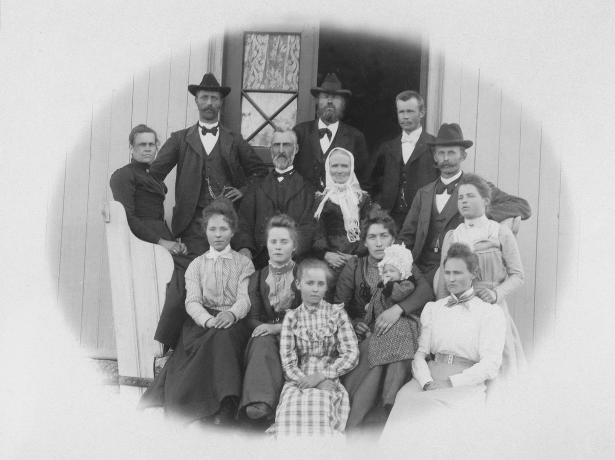 Stor familiegruppe på trappa ved hovedinngangen på Aske mellem, Nes, Hedmark. I midten er Anders Larsen Storlien (1838-1916) og hustru Agnethe Simensdatter Tretengen (1849-1910). Simen Andersen Storlien (1873-1940) med hatt til høyre. Foran ham sitter hans kone Anna Eriksdatter Hovie (1875-1960) med datter Aslaug f.1900 på fanget. Til venstre står Lars Andersen Storlien f. 1868 med hatt og hans kone Karen sitter ved siden av ham. De to som står i døråpningen må være Hans (1875-1940) og Nils f.1878. Jentene må være Anne f.1870, Hilda f.1880, Anette Helene f.1882, Syverine f.1884 og Gunda f.1887.