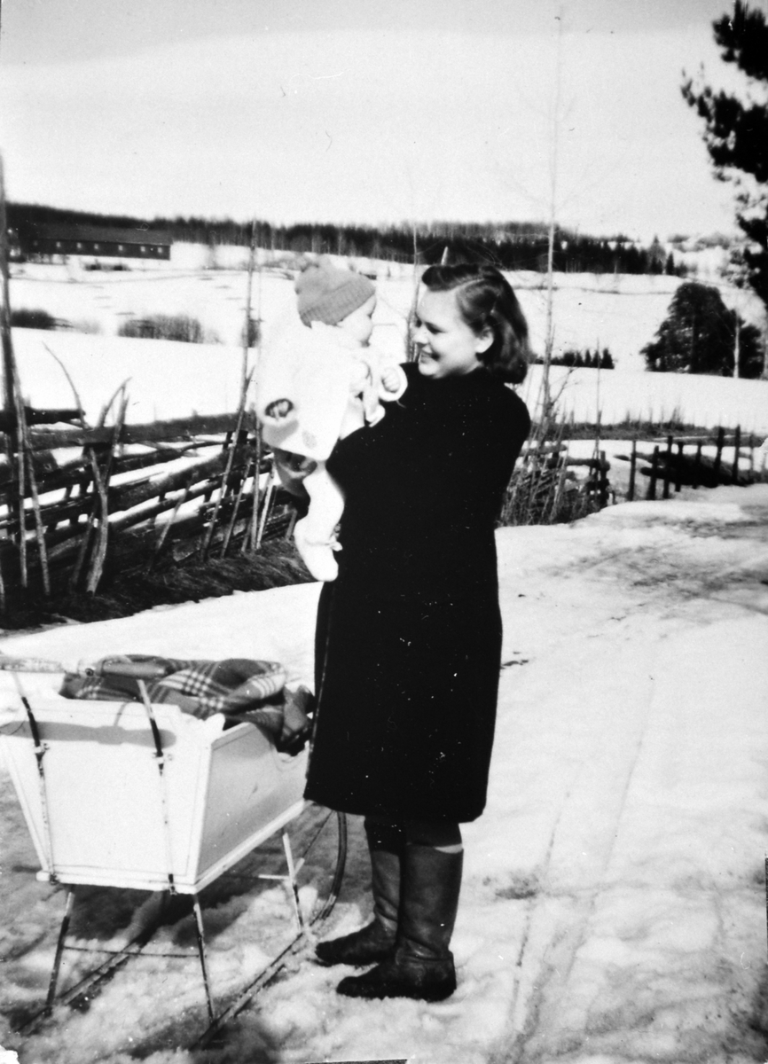 En vårdag langs Præstvægen. Tokstad gård i bakgrunnen. Tokstadfurua i kanten til høyre. Ukjente dame med barn og sluffe. Skigard.