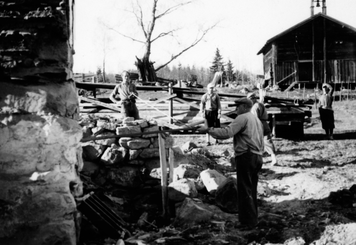 Grunnarbeid og muring. Førådsbygningen er revet (1952) og grunnarbeid for den nye hovedbygningen forberedes. Gardbruker Hans Medlien i forgrunnen. Stabburet fra 1700-tallet i bakgrunnen.