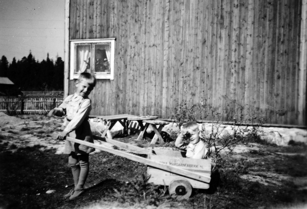 Oddvar Vestli drar broren Terje Vestli i "stuttkjerre" foran Solly på Ilseng. Barneleke, kjerre laget av smørkasse. Ca. 1946. 