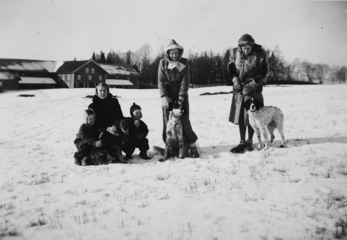 Gruppe 5 + 3 hunder ute på jordet, med Atlungstad gård i bakgrunn. Vinter. 
