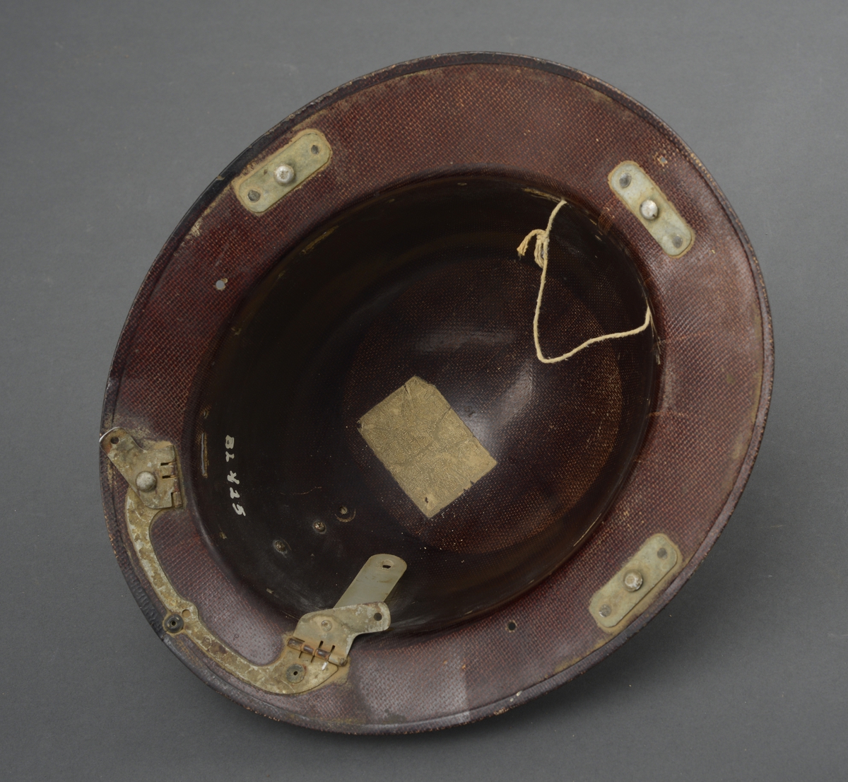 Gruvehjelm med påsatt del avplast og jern for feste av skjerm på undersiden av bremmen. Lampefeste på front- og ledningsfeste bak på hjelmen.