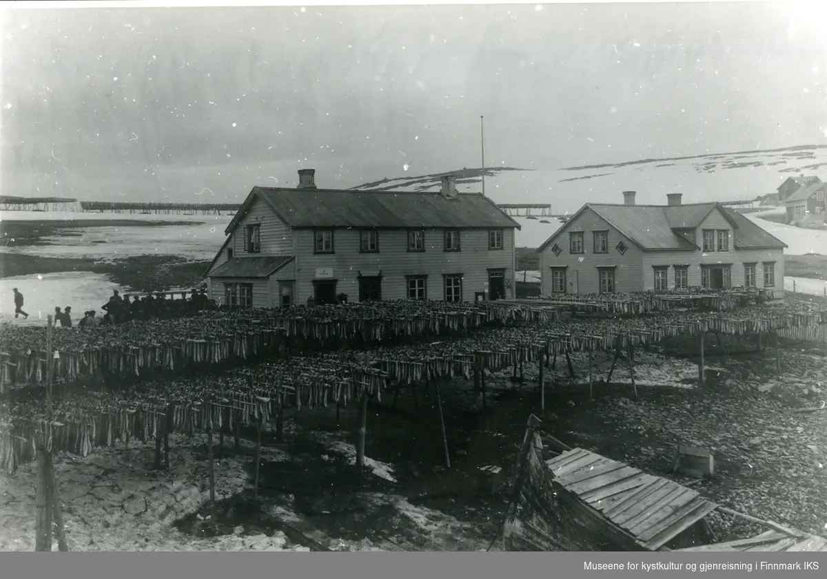 Fullhengte fiskehjeller i forgrunnen, to bygninger tilhörende B.T Aas i bakgrunnen. Vi ser hovedgården til høyre med telegraf, i den andre bygningen er det butikk og postkontor.