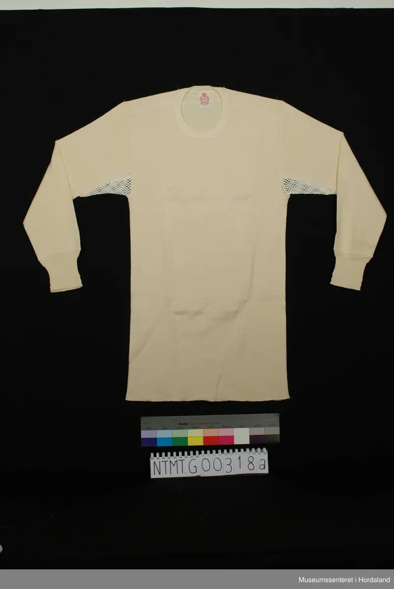 Lange ermer med brotavslutning, rund hals, skulderstykke, kile med helsetrøyestoff under ermer.