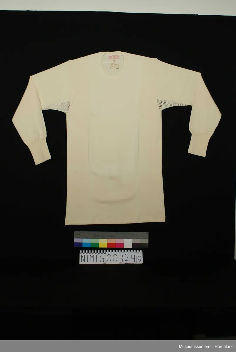 Rund hals, lange ermer med brotavslutning, kile under ermer, skulderstykker.