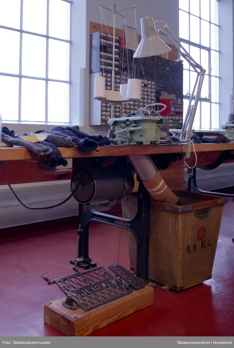 Mingrøn 1-nåls overlockmaskin som syr saman to delar trikotstoff, og samtidig kuttar av overflødig stoff med ein kniv. Maskina har tre trådar, men ein kan òg tre den med to trådar. Den har ei pumpe som oljar maskina automatisk.

Maskina er montert på eit Singer-bord saman med fleire andre symaskiner etter at den kom til museet. Bordet har eit hol der kappet frå symaskinene skulle dette ned.