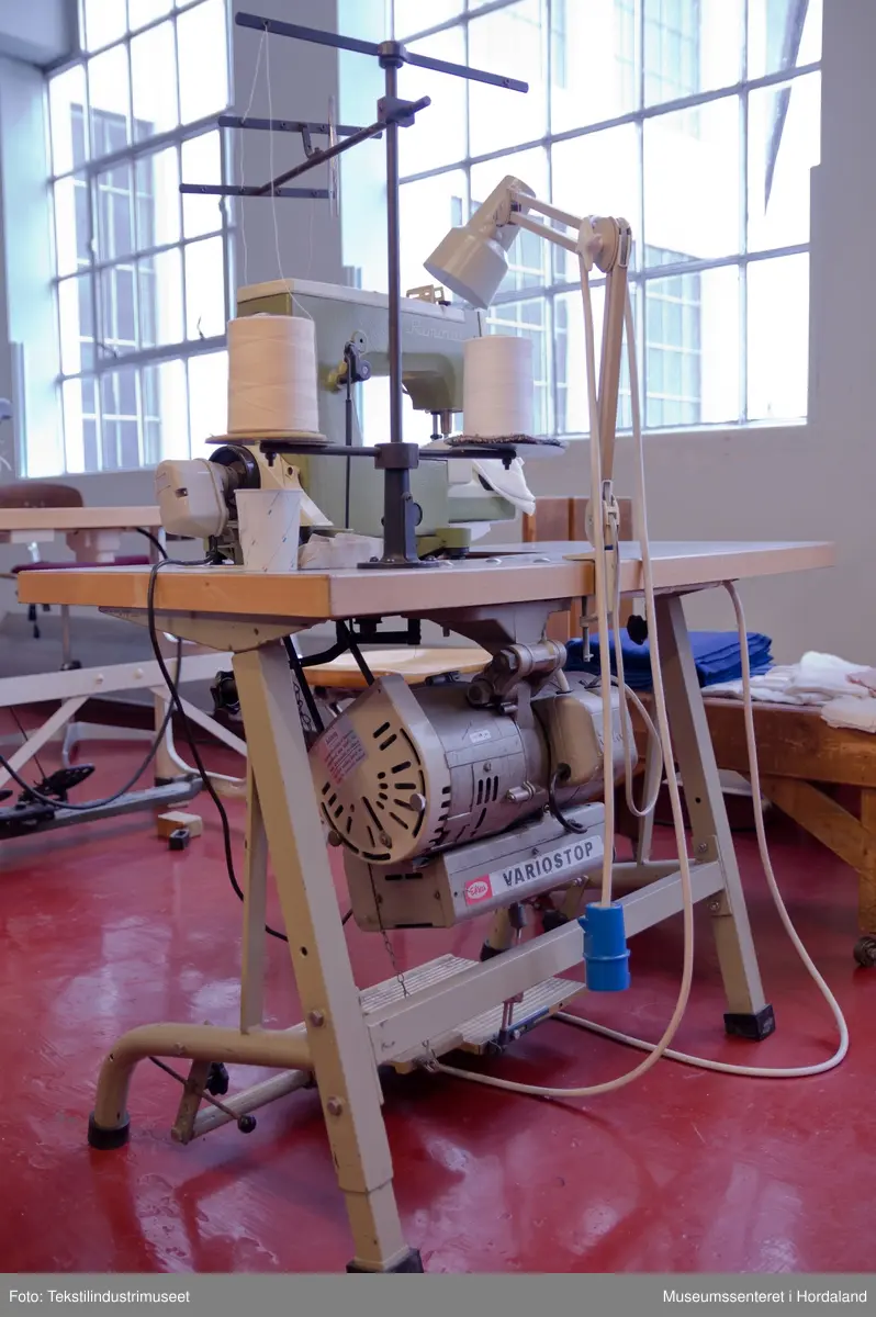 Rimoldi-symaskin montert på lite bord med pedalar og motor under bordet, og stativ til to trådsneller og trådførarar ved sidan av maskina. Strømbrytar er plassert under bordet.

Motor: Etka Variostop
Typ: VD 12
Nr. 08315789
3~Mot (triangel)Y 220/380 V
2,6 / 1,5 A     550 W
2800 / 3400 1/min
...
Made in Western Germany