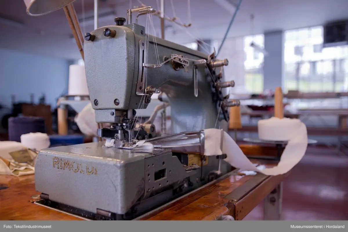 Rimoldi-symaskin som syr kantband til klede av strikka tekstilar (trikotasje). Ein kan sy med to og tre nåler og ein dekktråd. Ein tråd under ("looper"). Ein brukar band som er kutta til på ei anna maskin og rulla opp, plasserer ein enden av bandet i eit bandapparat i metall. Det blir så mata gjennom dette og sydd. 
Maskina er av klasse 1363 - 25.