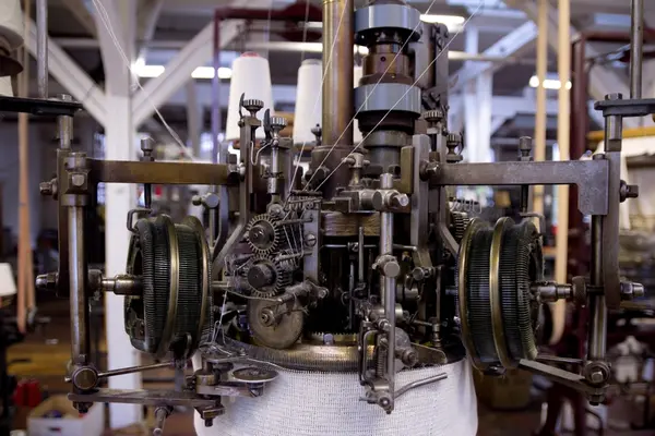 Rundstrikkemaskin/rundstol som er montert med eit feste og er kopla til reimdrift i taket. Maskina har tre system og ei nedtrekksmekanisme nederst med små metallpiggar montert på tekstilt materiale.